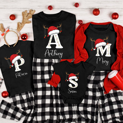 May include: A collection of black t-shirts and a baby bodysuit featuring white letters topped with red Santa hats and reindeer antlers. Each garment displays a name in white script: Anthony, Mary, Patricia, and Susan. The set includes black and white plaid pajama pants and a red cardigan.