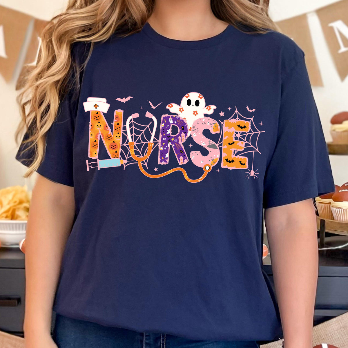 May include: Navy blue t-shirt with the word "NURSE" in a Halloween-themed design. The letters are decorated with pumpkins, spiderwebs, and a ghost. A stethoscope and syringe are also included in the design.