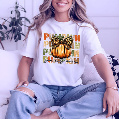 May include: White t-shirt with a pumpkin graphic. The graphic features an orange pumpkin with a leopard print bow and the words "PUMPKIN SEASON" in orange, green, and black. The shirt is a short-sleeved crew neck.
