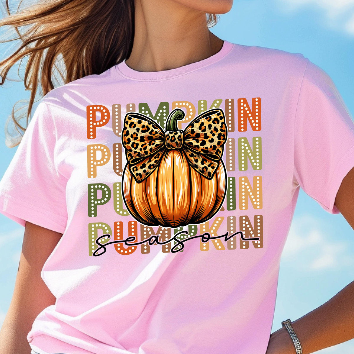 May include: Pink t-shirt featuring a large orange pumpkin with a leopard print bow. The word "PUMPKIN" is stacked vertically in orange, green, and yellow. The words "SEASON" are written in a script font.