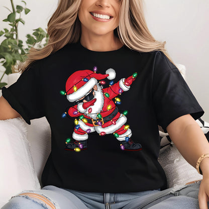 May include: Black t-shirt featuring a cartoon Santa Claus dabbing. Santa is wearing a red suit, hat, and sunglasses, with a white beard and trim. Colorful Christmas lights are draped around him. The design is centered on the shirt.