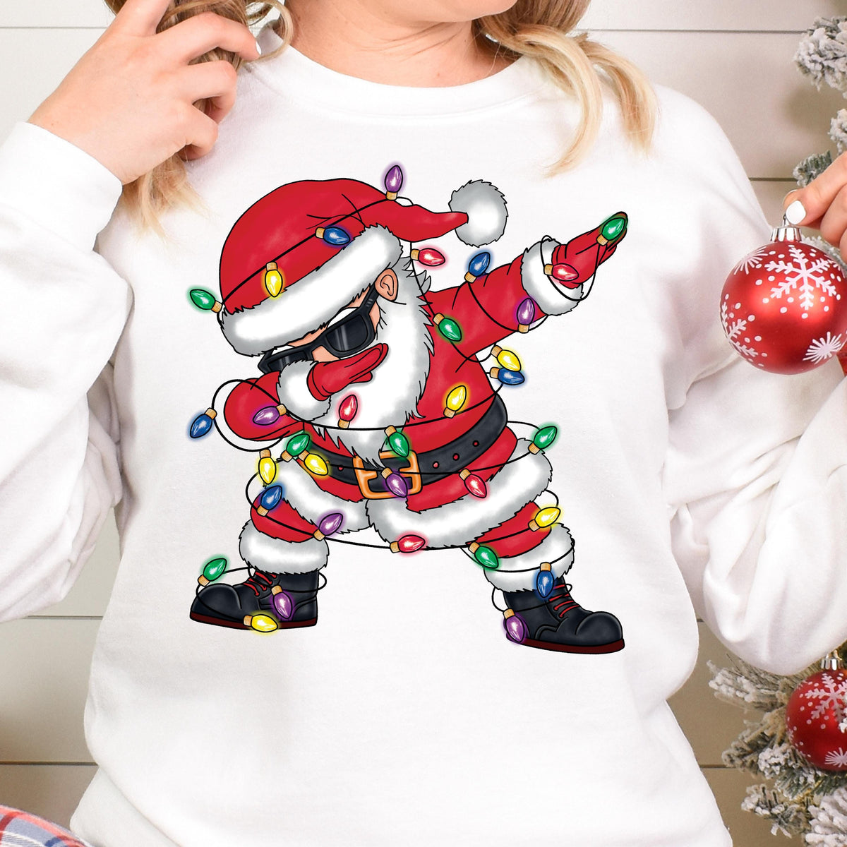 May include: White sweatshirt with a cartoon image of Santa Claus wearing sunglasses and tangled in Christmas lights. Santa is in a dabbing pose.