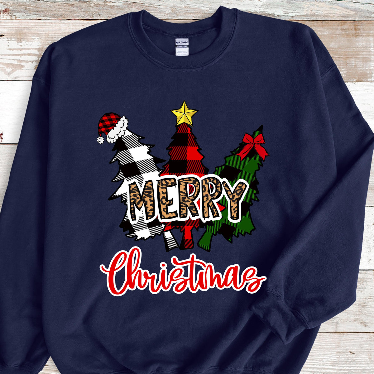 May include: A navy blue crewneck sweatshirt featuring a graphic of three stylized Christmas trees. The trees have black and white buffalo plaid, red and black plaid, and green patterns. The word MERRY is in leopard print, and Christmas is in red script.