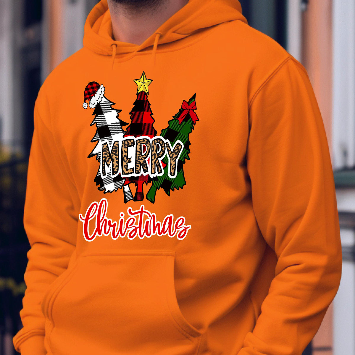 May include: An orange hooded sweatshirt featuring a graphic of three stylized Christmas trees with buffalo plaid patterns in black, white, and red. The word Merry is printed in a leopard print font, and the word Christmas is in red script.
