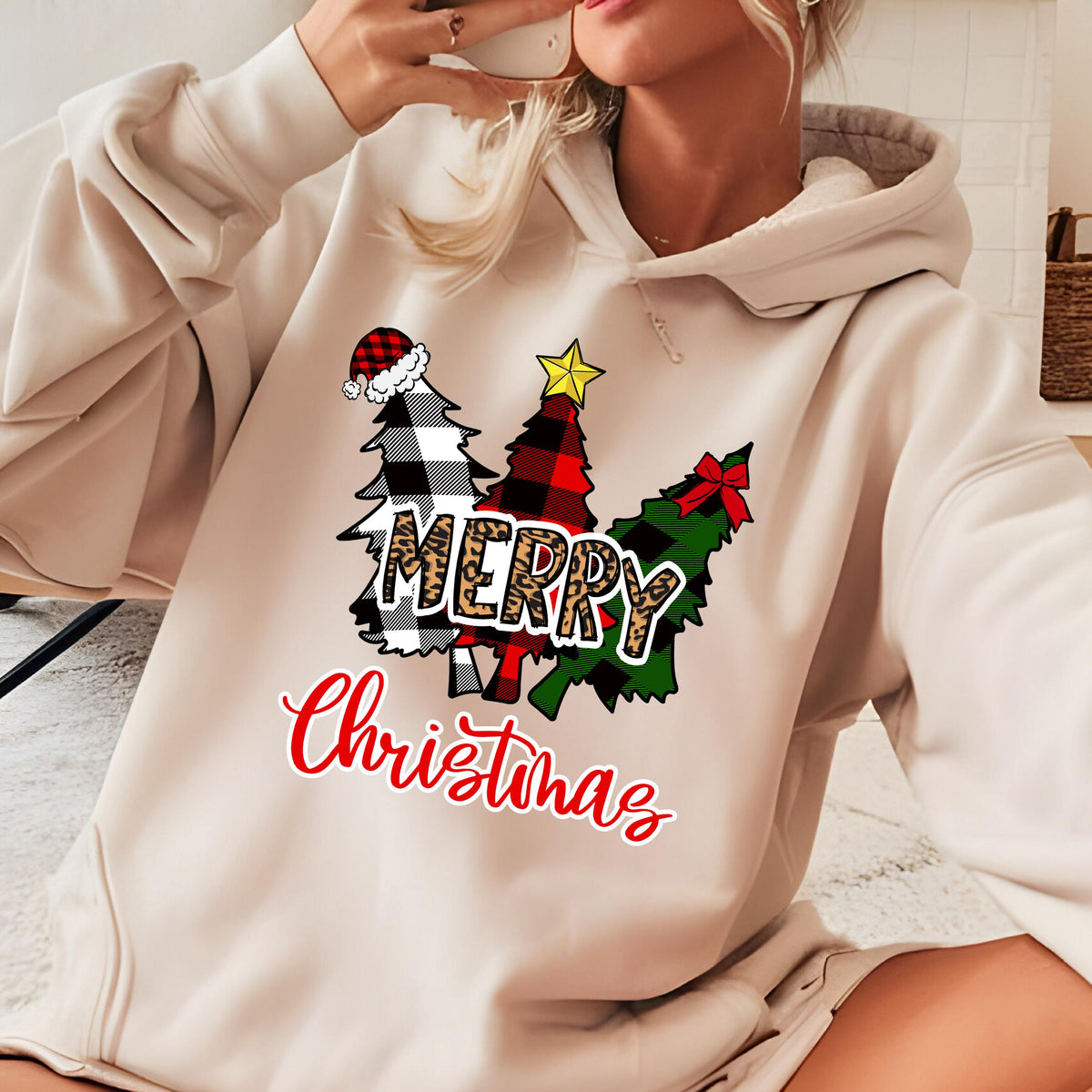 May include: A beige hooded sweatshirt featuring a graphic of three stylized Christmas trees in black and white buffalo plaid, red and black plaid, and green plaid. The word MERRY is in leopard print, and the word Christmas is in red script.