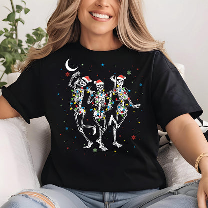 May include: Black t-shirt featuring a festive design of three dancing skeletons wearing Santa hats and wrapped in colorful Christmas lights. A crescent moon and snowflakes complete the holiday theme.