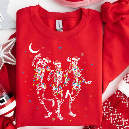 May include: A bright red crewneck sweatshirt featuring a graphic of three white skeletons wearing red Santa hats. The skeletons are wrapped in colorful Christmas lights and are dancing under a white crescent moon and small colorful stars.