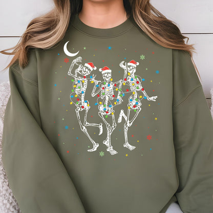 May include: An olive green crewneck sweatshirt featuring a graphic of three white skeletons wearing red Santa hats. The skeletons are wrapped in colorful Christmas light strings, surrounded by small stars, snowflakes, and a white crescent moon.