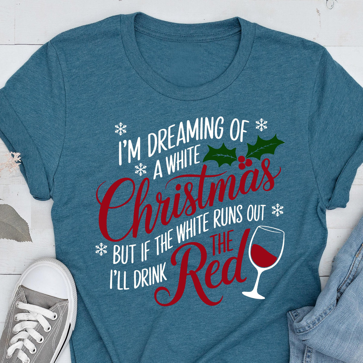 May include: Teal t-shirt with the text "I'M DREAMING OF A WHITE Christmas BUT IF THE WHITE RUNS OUT I'LL DRINK THE RED" in white and red. The design includes snowflakes, holly, and a wine glass.