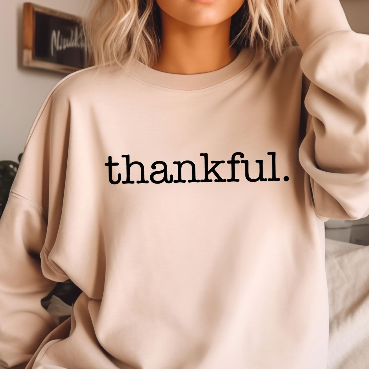 May include: A beige sweatshirt with the word "thankful" printed in black, centered on the front. The long-sleeved top is made of a soft material and is suitable for casual wear. The sweatshirt has a crew neck.