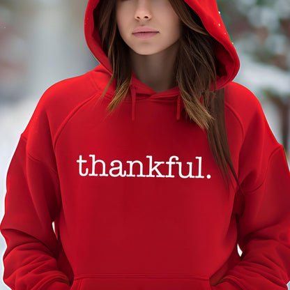 May include: A red hooded sweatshirt with the word "thankful." printed in white. The sweatshirt has a drawstring hood and a front pocket. The background is blurred, suggesting an outdoor setting.