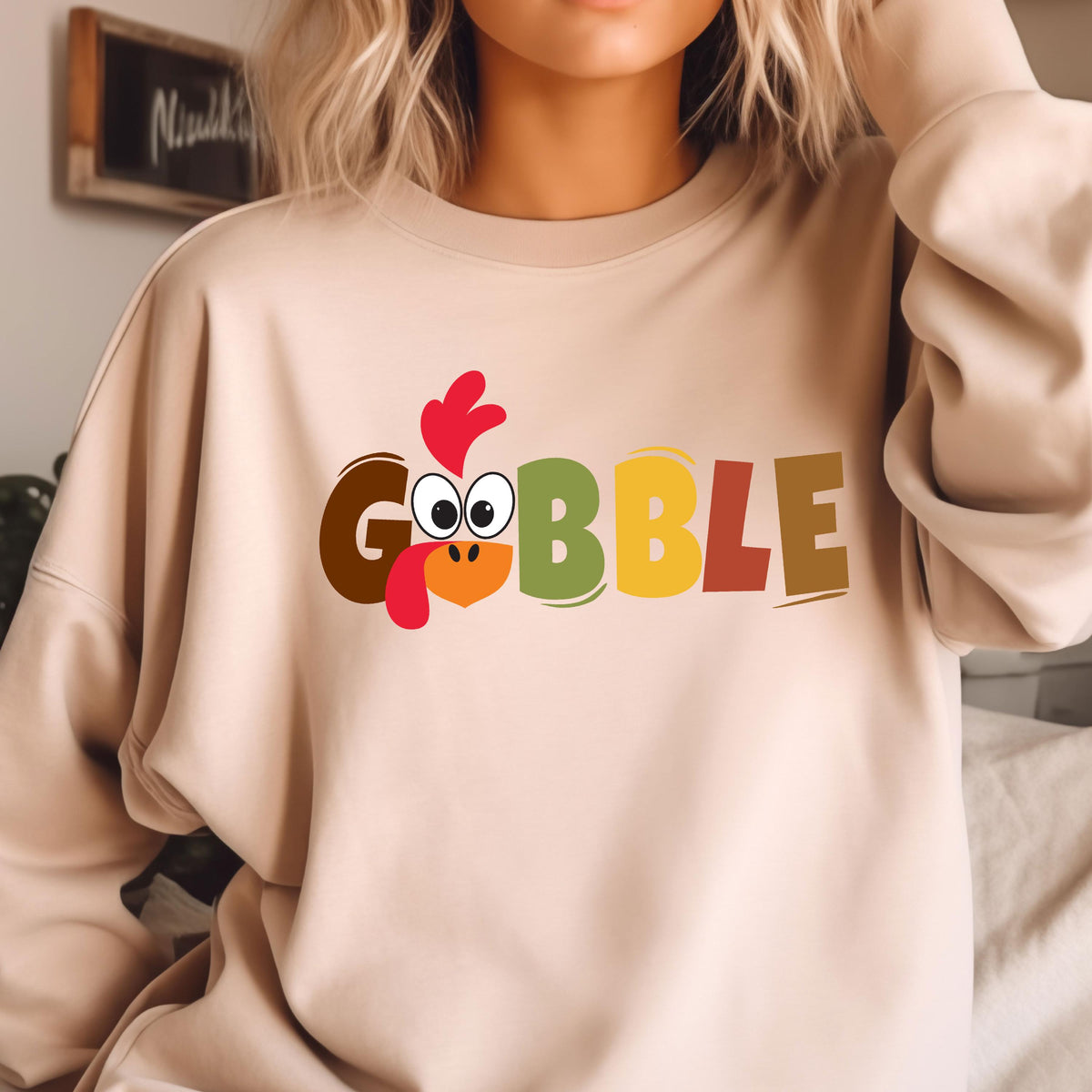 May include: A beige sweatshirt with a graphic of a turkey head and the word "GOBBLE" in colorful letters. The turkey head is brown, red, and yellow. The letters are brown, red, yellow, green, and orange.