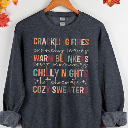 May include: A dark gray sweatshirt with a colorful graphic print that reads "Crackling Fires, Crunchy Leaves, Warm Blankets, Crisp Mornings, Chilly Nights, Hot Chocolate, Cozy Sweaters".
