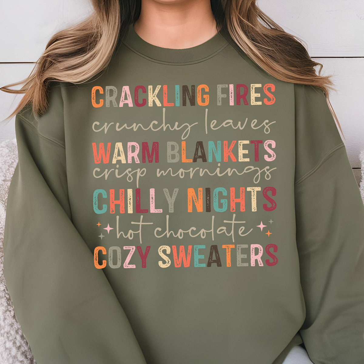 May include: A green sweatshirt with the text "Crackling Fires, crunchy leaves, Warm Blankets, crisp mornings, Chilly Nights, hot chocolate, Cozy Sweaters" in colorful, stylized lettering.
