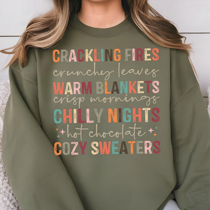 May include: A green sweatshirt with the text "Crackling Fires, crunchy leaves, Warm Blankets, crisp mornings, Chilly Nights, hot chocolate, Cozy Sweaters" in colorful, stylized lettering.