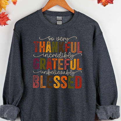 May include: A dark heather gray crewneck sweatshirt featuring the text so very THANKFUL incredibly GRATEFUL unbelievably BLESSED in a multi-colored, distressed font. The words are arranged in a stacked design with autumn-inspired colors.
