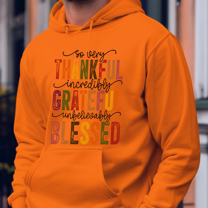 May include: A bright orange hooded sweatshirt featuring a front graphic with the text so very THANKFUL incredibly GRATEFUL unbelievably BLESSED. The words are printed in a mix of script and block fonts using various autumn-inspired colors.