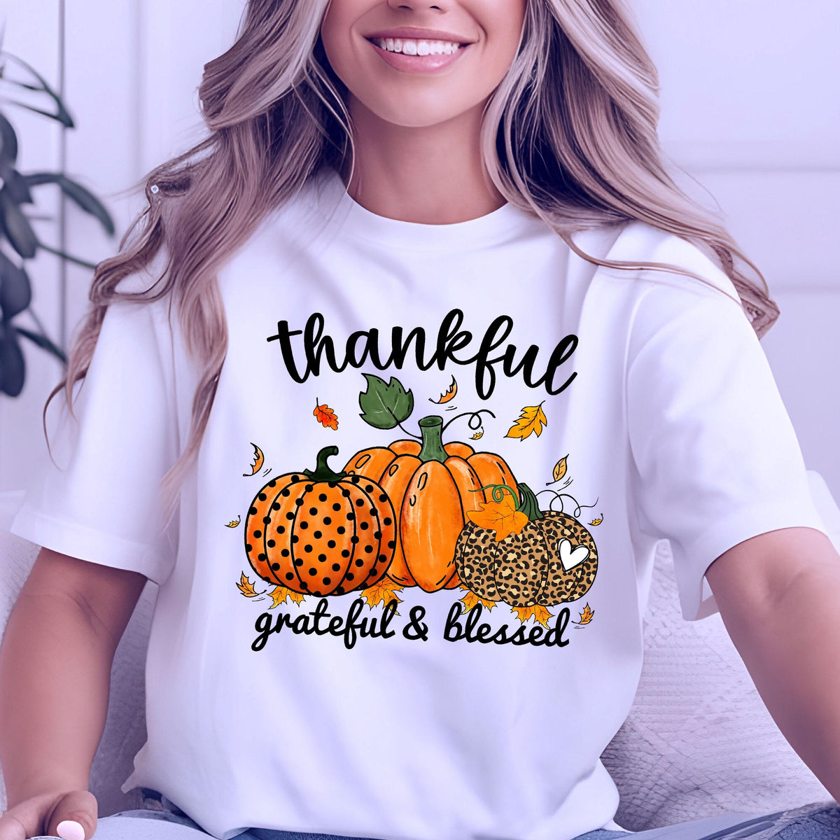 May include: White t-shirt with a fall-themed graphic. The design features three pumpkins in orange and leopard print, surrounded by falling leaves. The words "thankful, grateful & blessed" are written in black script.