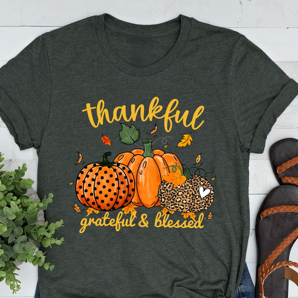 May include: Dark gray t-shirt with a fall-themed graphic. The design features orange pumpkins, fall leaves, and the words "thankful, grateful & blessed" in yellow script. The pumpkins have various patterns.