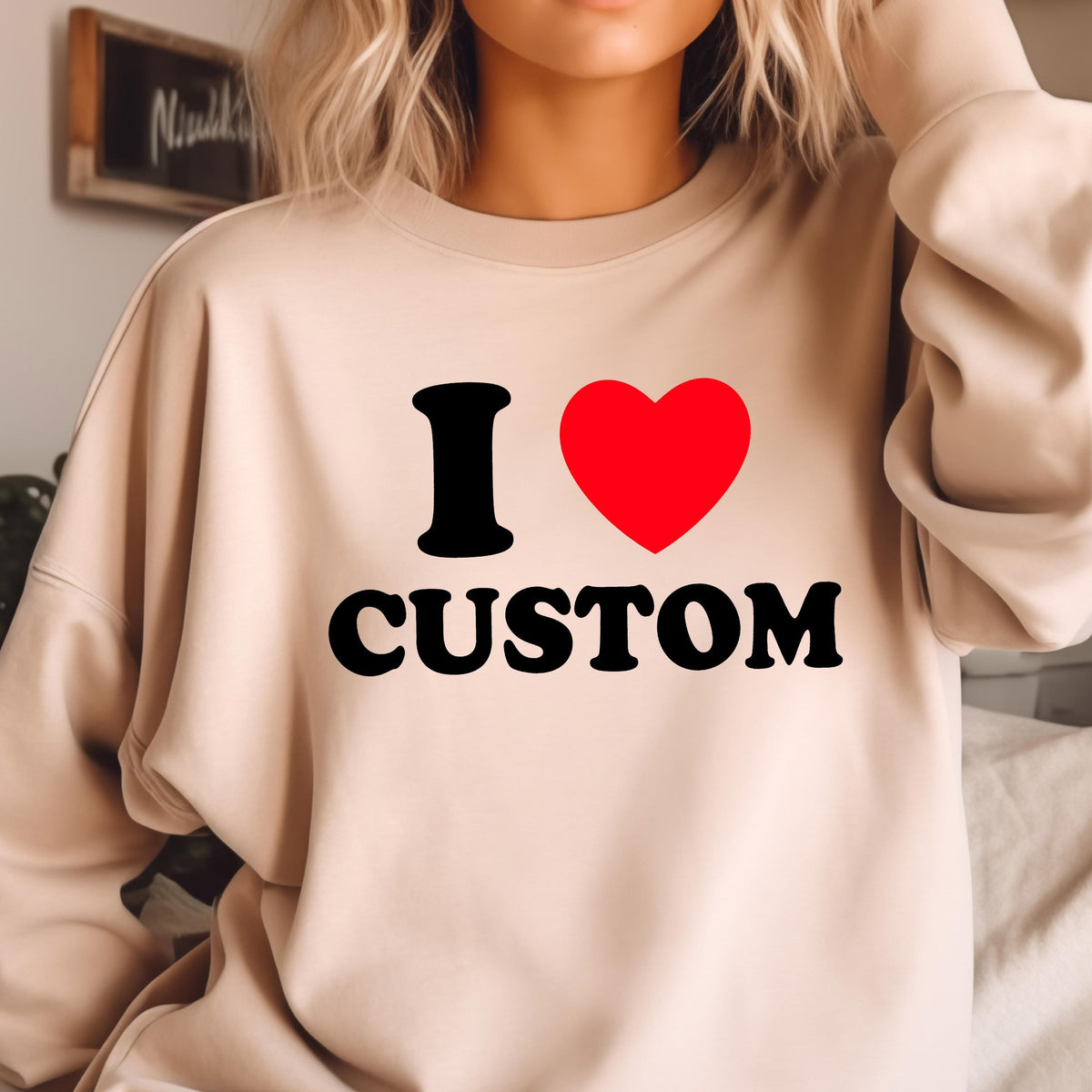 May include: A beige sweatshirt with the text "I ♥ CUSTOM" in black and red. The "I" is black, the heart is red, and "CUSTOM" is in a bold, black font. The sweatshirt is a neutral color.