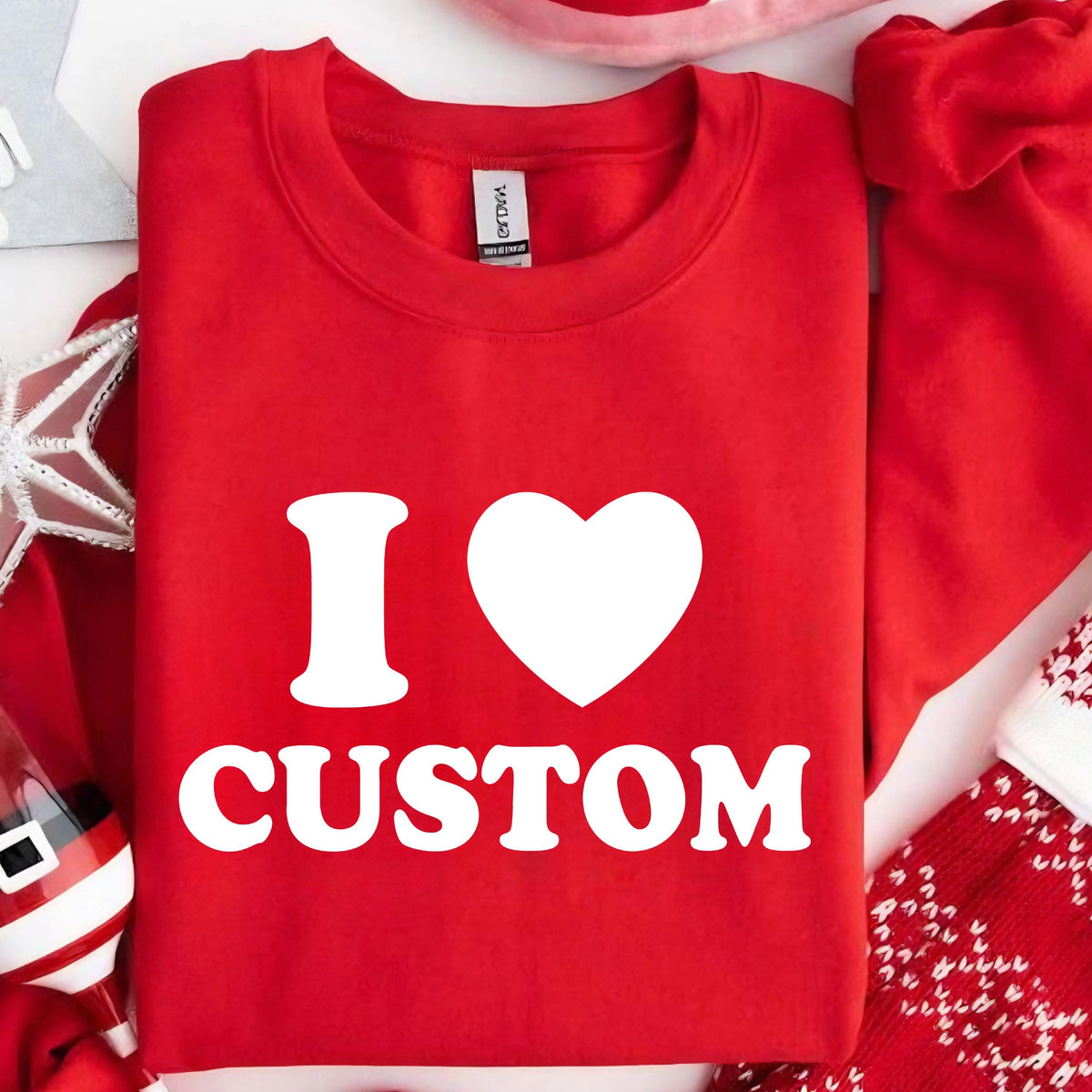 May include: A red crew neck sweatshirt with the text "I ♥ CUSTOM" in white. The heart symbol replaces the word "love". The sweatshirt is displayed on a white surface with holiday decorations.