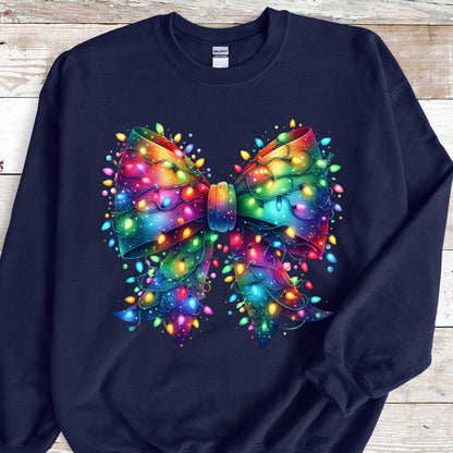 May include: A navy blue crewneck sweatshirt featuring a large, central graphic of a decorative bow. The bow is rendered in a vibrant, multi-colored gradient and is intricately wrapped with glowing, multi-colored string Christmas lights.