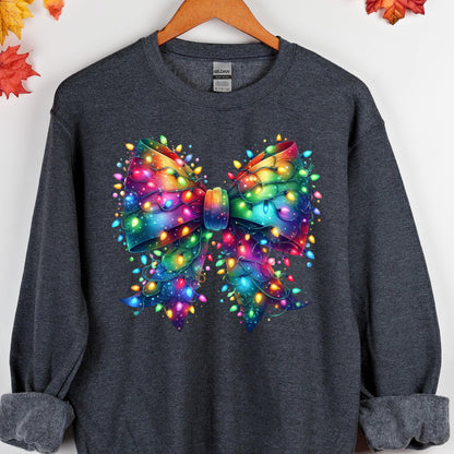 May include: A dark charcoal gray long-sleeve sweatshirt featuring a large, central graphic of a bow made entirely of glowing, multi-colored Christmas string lights. The lights appear in vibrant shades of red, blue, green, yellow, and purple.