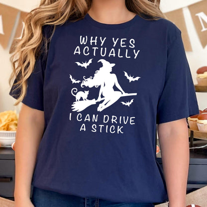 May include: Navy blue t-shirt with a white graphic of a witch on a broom, surrounded by bats, and the text "WHY YES ACTUALLY I CAN DRIVE A STICK". A Halloween-themed shirt.