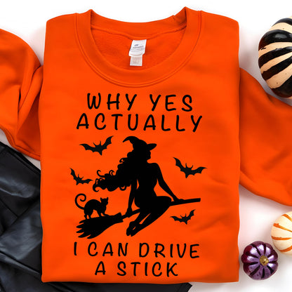 May include: An orange crewneck sweatshirt featuring a black graphic of a witch riding a broomstick with a cat and bats. The text reads: WHY YES ACTUALLY I CAN DRIVE A STICK. The design is centered on the front of the garment, which has a white tag.