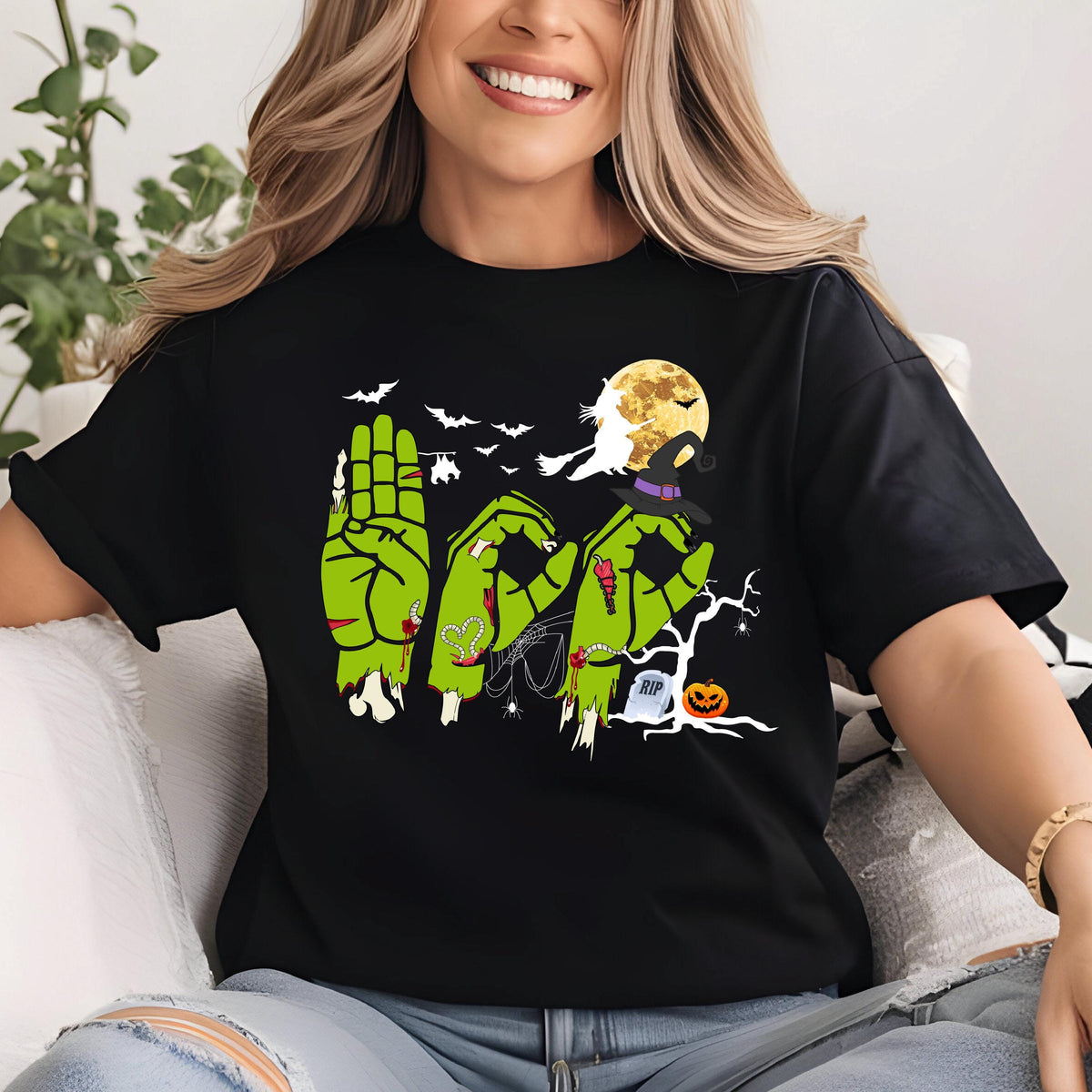 May include: A black t-shirt featuring a graphic of three green zombie hands spelling out the word BOO in American Sign Language. The design includes a yellow full moon, a flying witch silhouette, bats, a spider web, a tombstone, and a pumpkin.