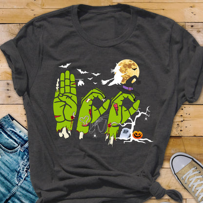 May include: A dark gray t-shirt featuring a graphic of three green zombie hands forming the letters B, O, and O. The design includes a yellow full moon, a silhouette of a witch on a broomstick, bats, a spider web, a tombstone with RIP, and a jack-o'-lantern.
