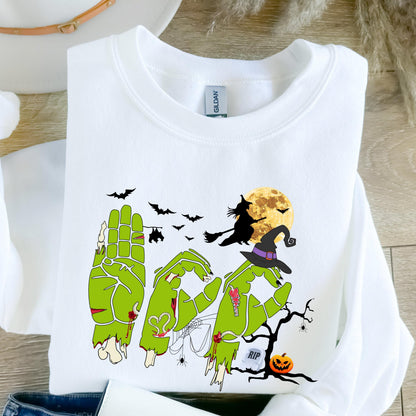 May include: White sweatshirt with a Halloween-themed graphic. The design features green zombie hands spelling out the word "BOO", a witch on a broom, bats, a full moon, and a jack-o'-lantern. The word "RIP" is also included in the design.