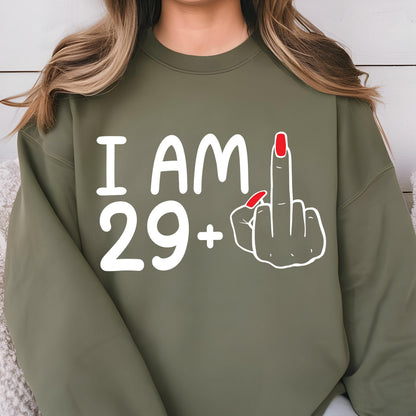 May include: Olive green sweatshirt with white text that reads "I AM 29+." A white outline of a hand giving the middle finger is to the right of the text. The middle finger has red nail polish.