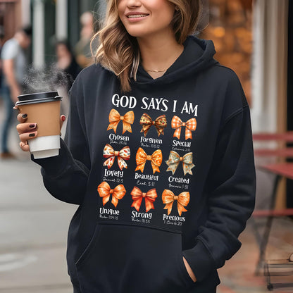 May include: A black hooded sweatshirt featuring the white text "GOD SAYS I AM" above nine colorful illustrated bows. Each bow is labeled with a descriptive word and a Bible verse reference, including Chosen, Forgiven, Special, Lovely, Beautiful, Created, Unique, Strong, and Precious.