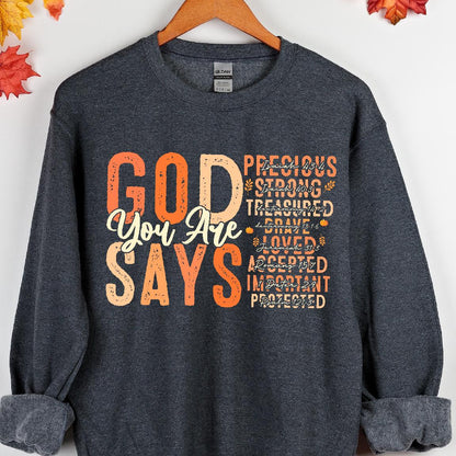May include: A dark gray sweatshirt with the text "GOD YOU ARE SAYS" in orange and white. The text is surrounded by a list of positive affirmations, including "precious", "strong", "treasured", "brave", "loved", "accepted", "important", and "protected".