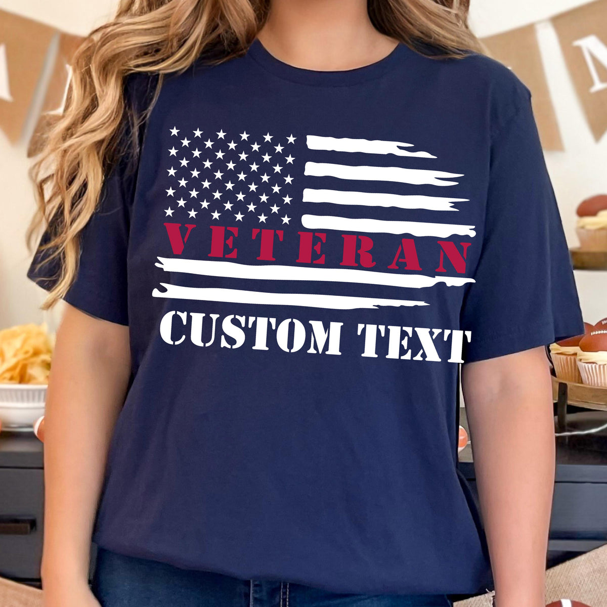 May include: Navy blue t-shirt featuring a distressed American flag design. The flag includes white stars and stripes, with the word "VETERAN" in red and "CUSTOM TEXT" in white. The shirt is a comfortable, casual style.