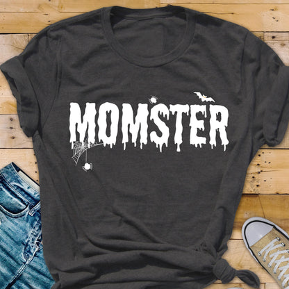 May include: Dark gray t-shirt with the word "MOMSTER" in white, dripping font. A spider web and spider are on the left, and a bat is above the "R". The shirt is folded at the bottom and has a casual style.