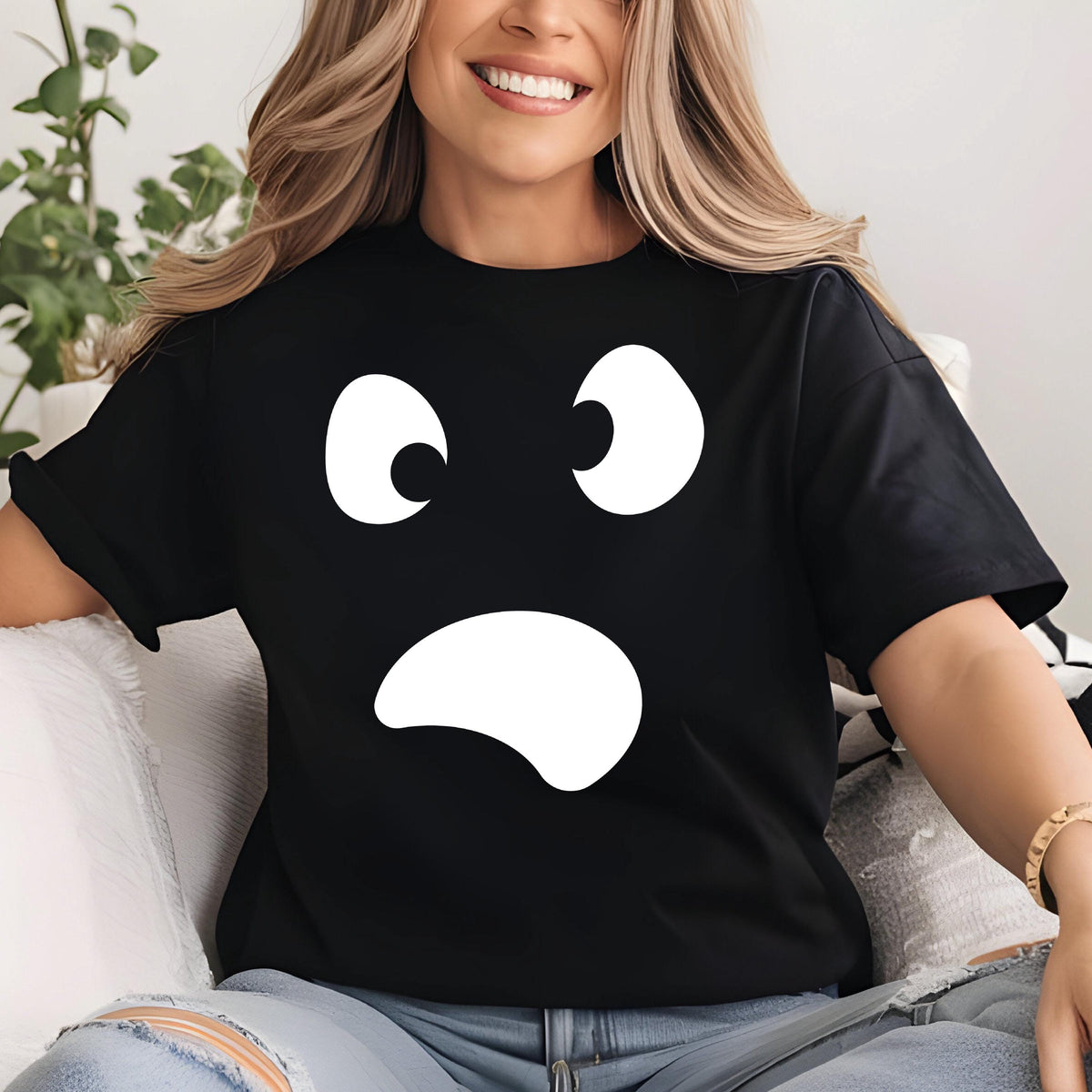 May include: Black t-shirt featuring a large white ghost face design. The graphic includes two oval eyes and a curved mouth, creating a simple, yet expressive design. The shirt is a classic crew neck style.