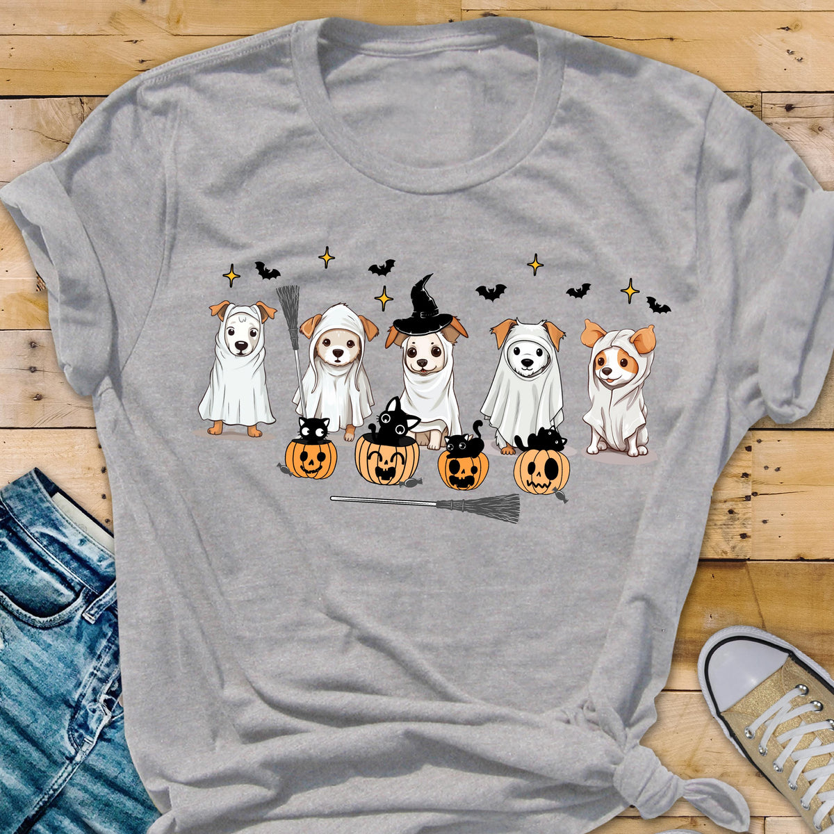May include: A light gray t-shirt featuring a graphic print of five dogs dressed as ghosts, with one wearing a witch hat. The design includes three orange jack-o'-lanterns with black cats, small black bats, and yellow stars scattered above the dogs.