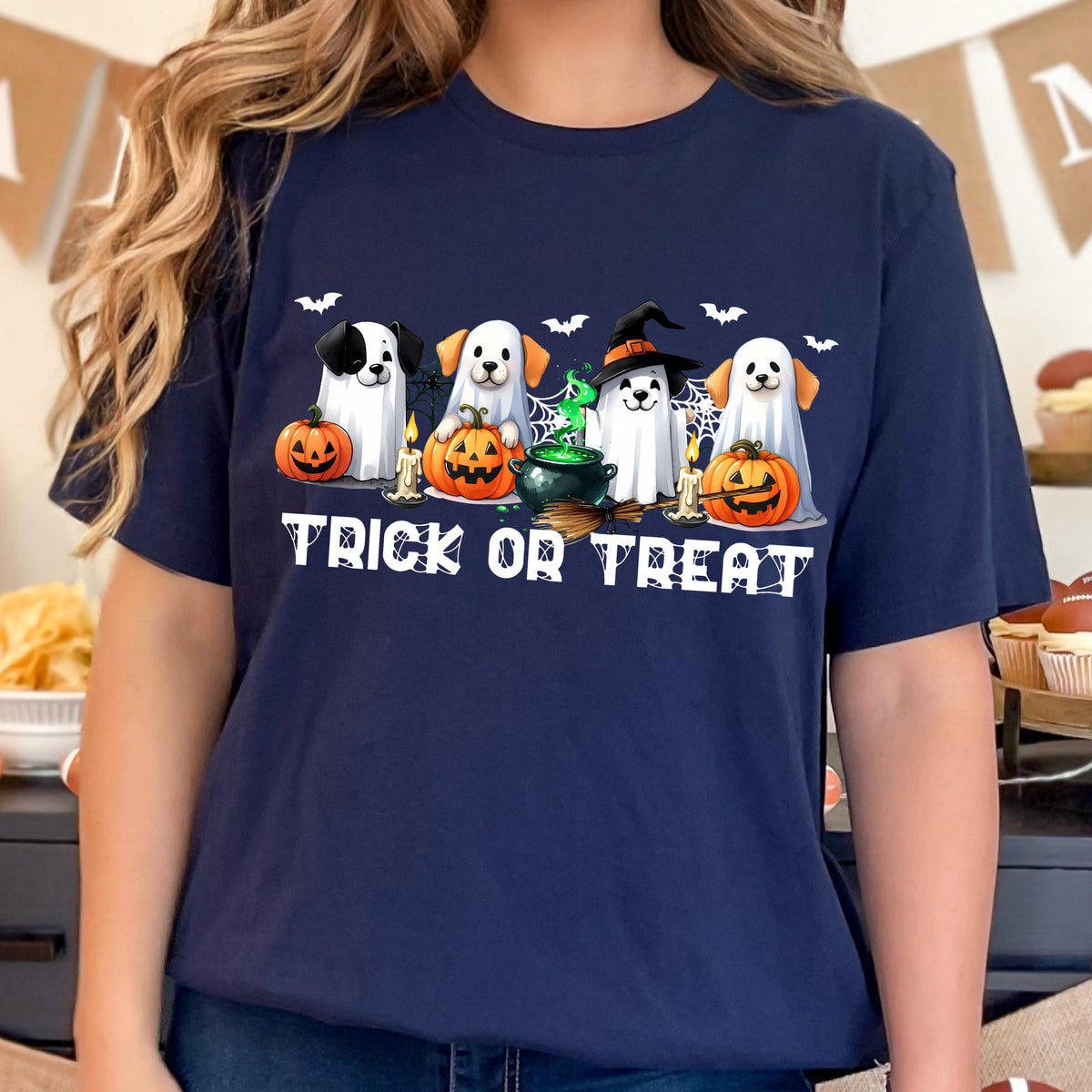 May include: A navy blue t-shirt featuring a graphic of four dogs dressed as ghosts for Halloween. The design includes orange pumpkins, a black cauldron with green liquid, lit candles, spider webs, and bats, with the text TRICK OR TREAT below.