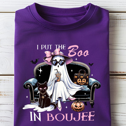 May include: A purple t-shirt featuring a graphic of a white ghost wearing a pink bow, hat, and sunglasses, sitting on a black sofa with a black cat, a pumpkin, and a handbag. The text reads I PUT THE BOO IN BOUJEE with small bats and stars.