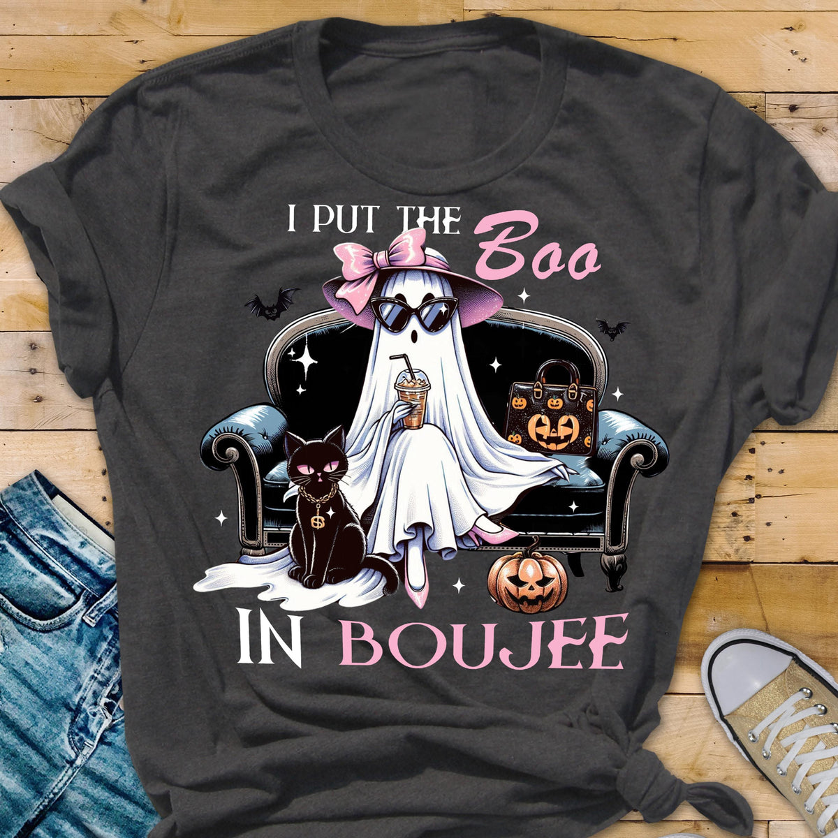 May include: A dark gray t-shirt featuring a graphic of a ghost wearing a pink bow, hat, and sunglasses, sitting on a sofa with a black cat, a pumpkin, and a handbag. The text reads I PUT THE BOO IN BOUJEE with small bats and stars surrounding it.