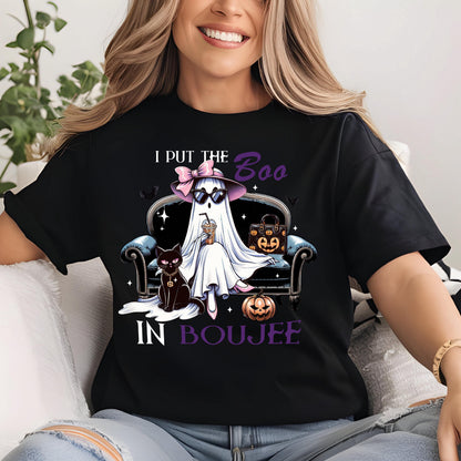 May include: A black t-shirt featuring a graphic of a ghost wearing a pink bow and sunglasses, sitting on a couch with a black cat and a pumpkin-patterned handbag. The text reads I PUT THE BOO IN BOUJEE in white and purple lettering.