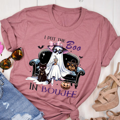 May include: A mauve short-sleeve t-shirt featuring a graphic of a ghost wearing a pink bow and sunglasses, sitting on a black sofa with a black cat and a pumpkin-patterned handbag. The text reads I PUT THE BOO IN BOUJEE with small bats.