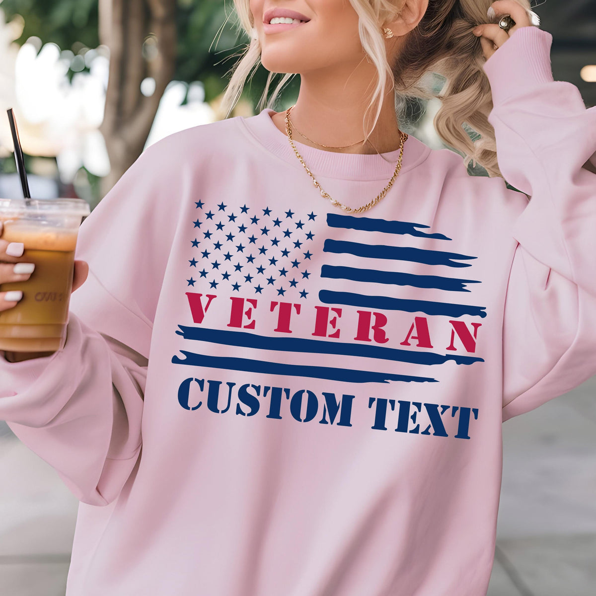 May include: A light pink sweatshirt featuring a stylized American flag design. The flag includes blue stars, red text reading "VETERAN," and the words "CUSTOM TEXT" in blue. The sweatshirt has long sleeves and a crew neck.