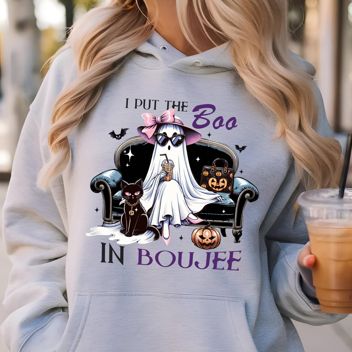 May include: A light gray hooded sweatshirt featuring a graphic of a ghost wearing a pink bow, sunglasses, and holding a coffee cup while sitting on a black sofa next to a black cat and a pumpkin, with the text I PUT THE BOO IN BOUJEE.