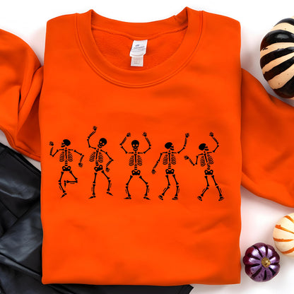 May include: An orange sweatshirt featuring a black graphic of five dancing skeletons. The skeletons are in various poses with their arms raised. The sweatshirt is a solid orange color, perfect for Halloween.