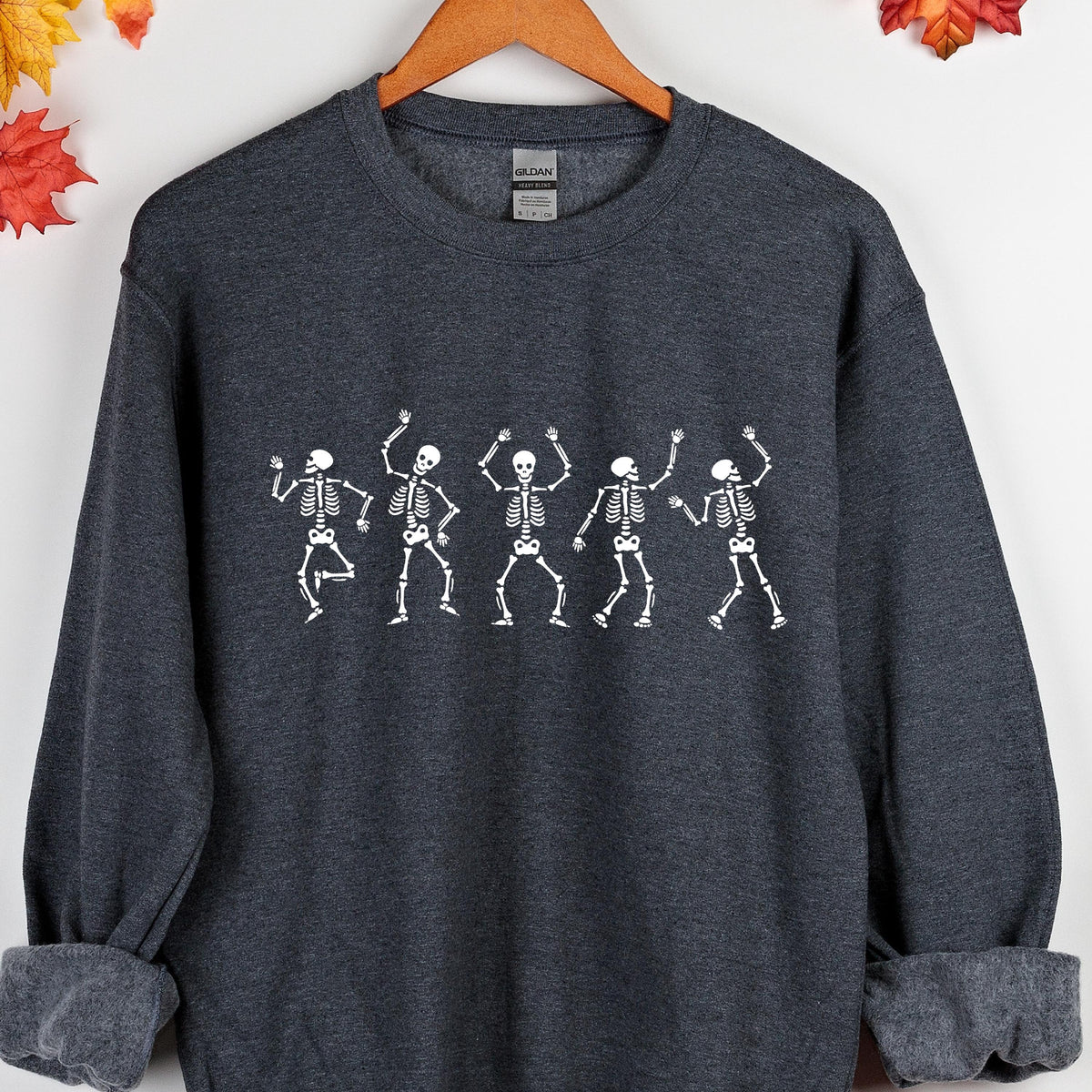 May include: Dark gray sweatshirt featuring a white graphic of five dancing skeletons. The skeletons are depicted with their arms raised in a celebratory pose. The sweatshirt has a crew neck and long sleeves with ribbed cuffs.