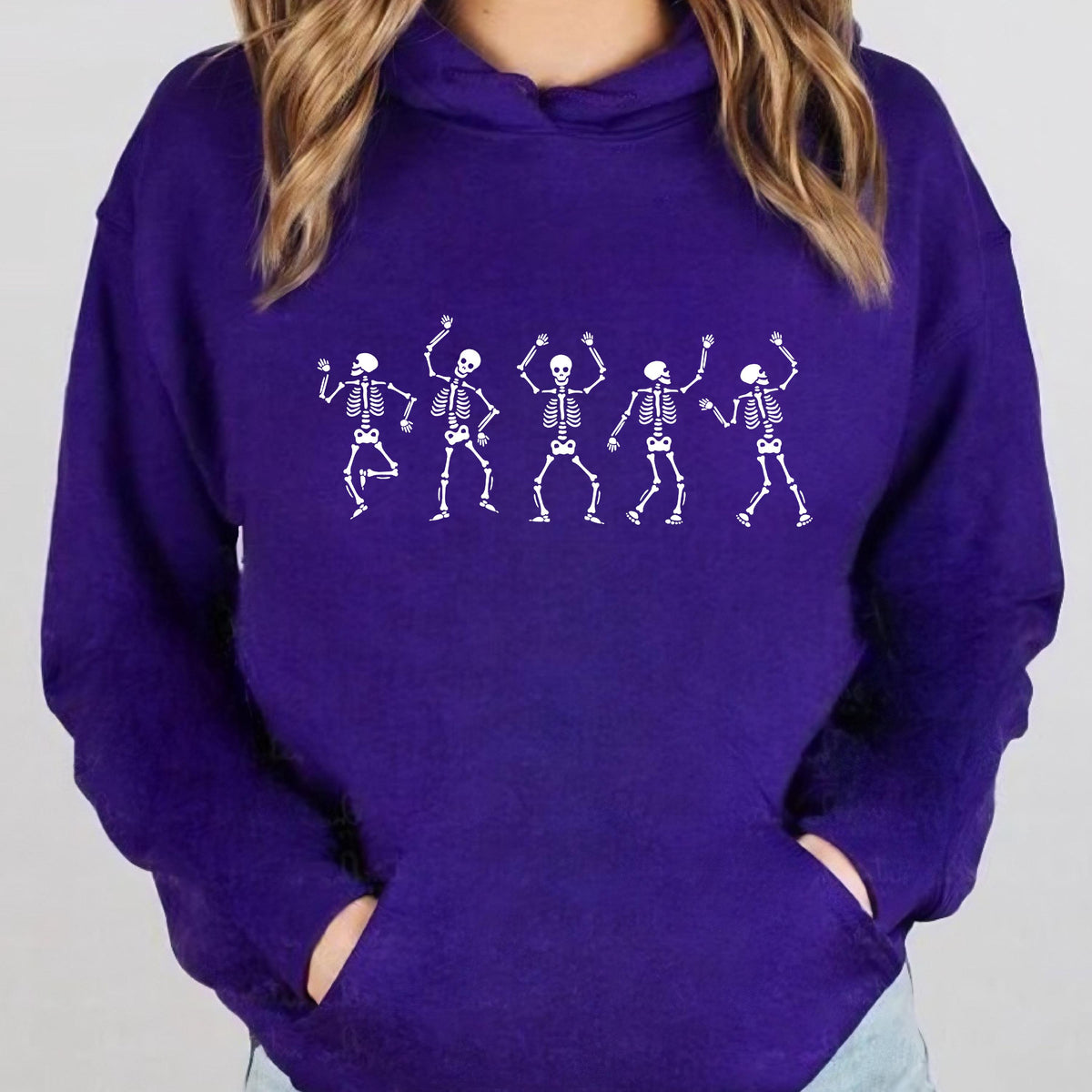 May include: A purple hoodie featuring a white graphic of five dancing skeletons. The skeletons are in various poses with their arms raised. The hoodie has a front pocket and a hood.