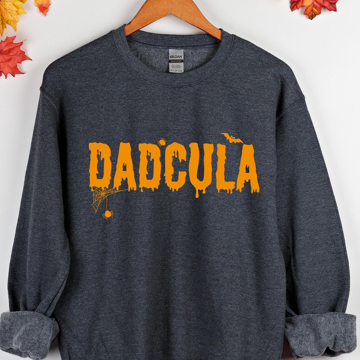 May include: A dark gray sweatshirt with the text "DADCULA" in orange dripping letters. The text is accompanied by a small spider web and a bat.